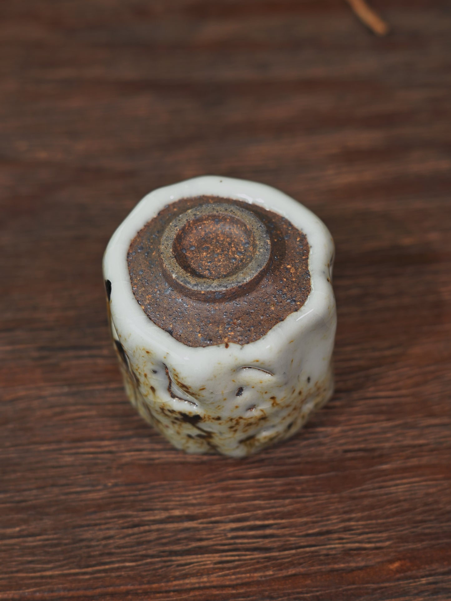 Artisan Shino teacup "Ashes Bloom" against a soft bokeh background with a traditional teapot.