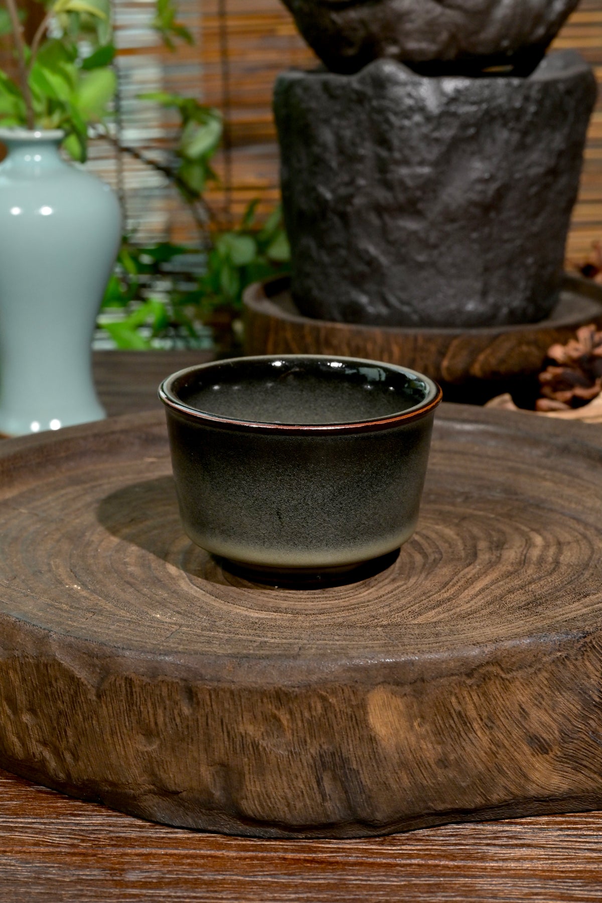 Traditional Longquan Ge kiln iron-clay tasting cup set against dark stone and bamboo background