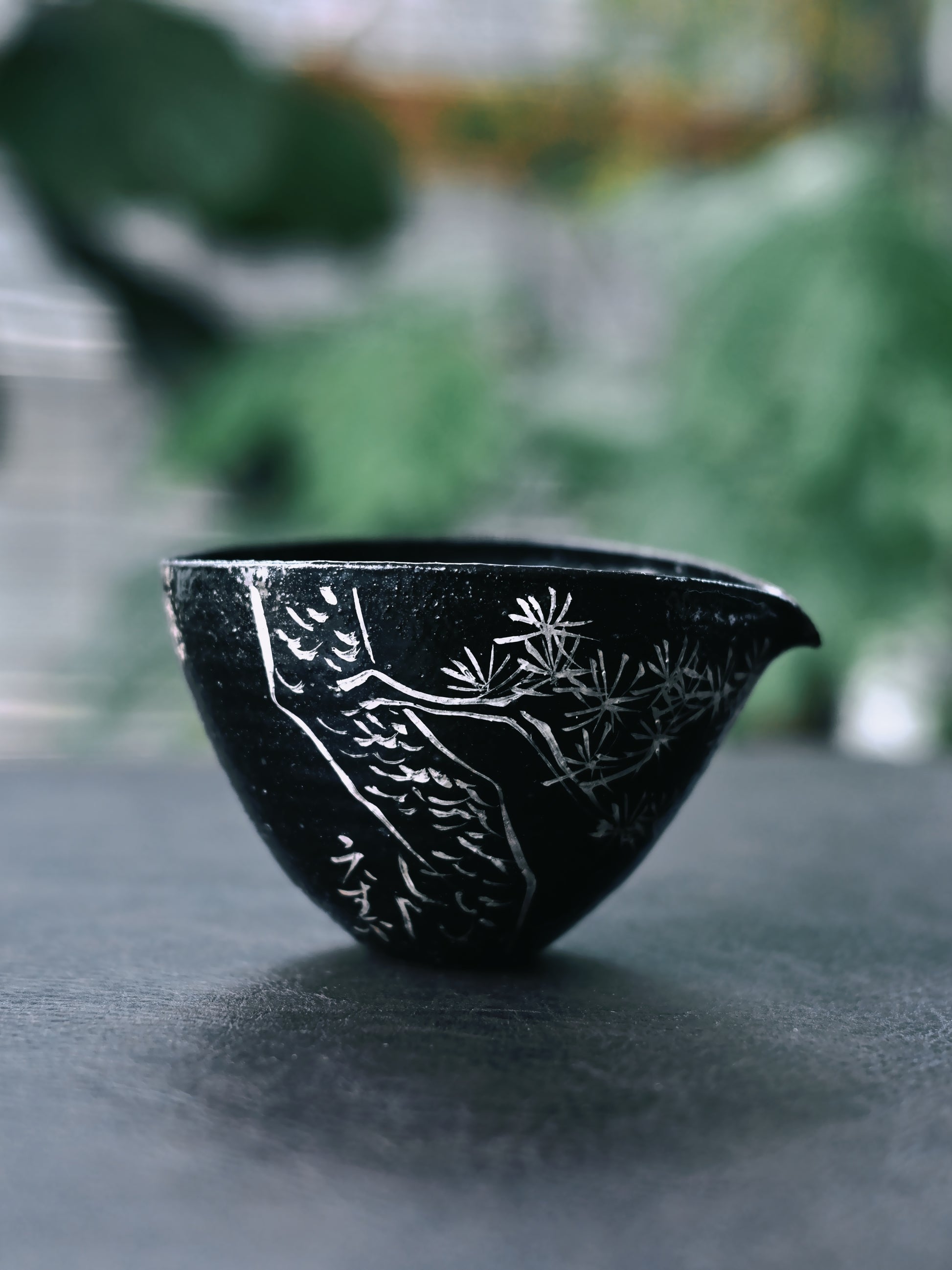Tactile wabi-sabi tea set: luminous black glaze contrasts with raised silver tracings of poetry and pines, inviting contemplation through texture and form.