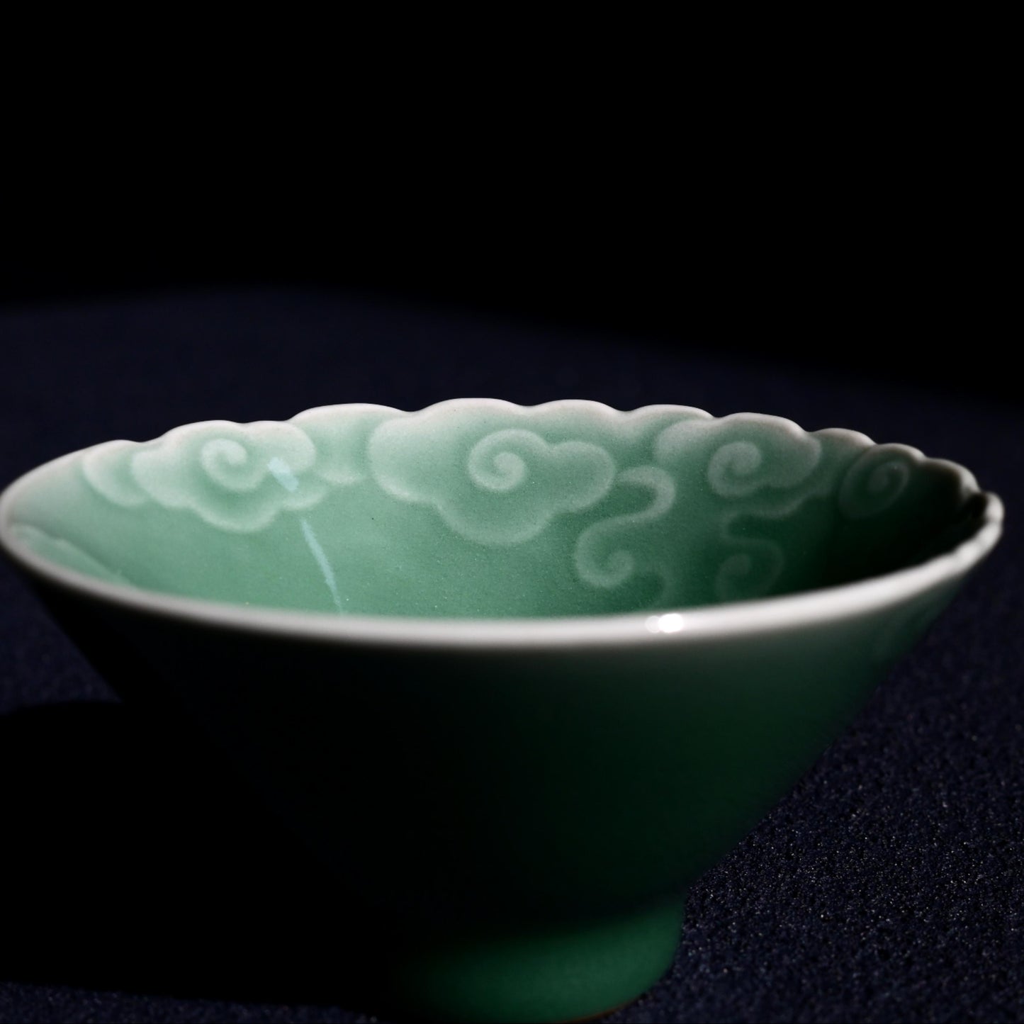Plum green glazed tea bowl with carved cloud motifs, representing ancient Chinese symbols of luck and happiness