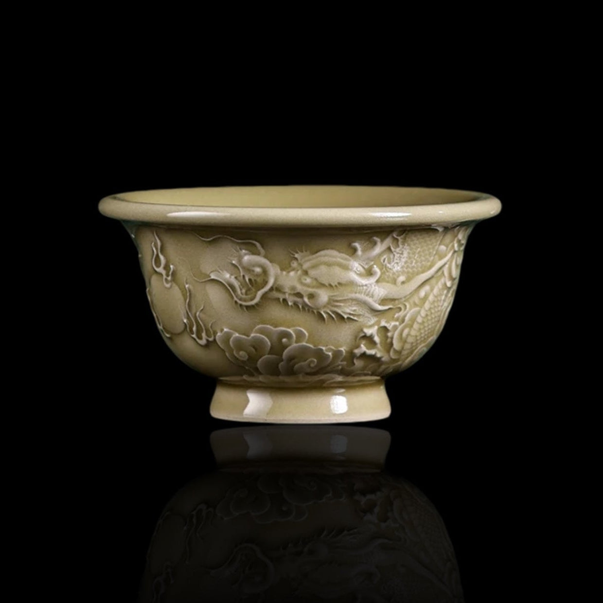 A close-up view of the Imperial Longquan Celadon tea cup featuring intricate hand-carved dragon relief against a dark green gradient background.