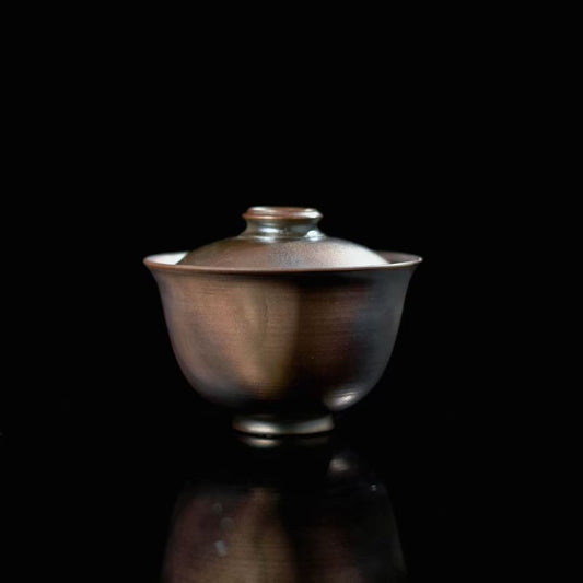 Unique handmade wood-fired iron clay Gaiwan on a traditional wooden carved tea table.