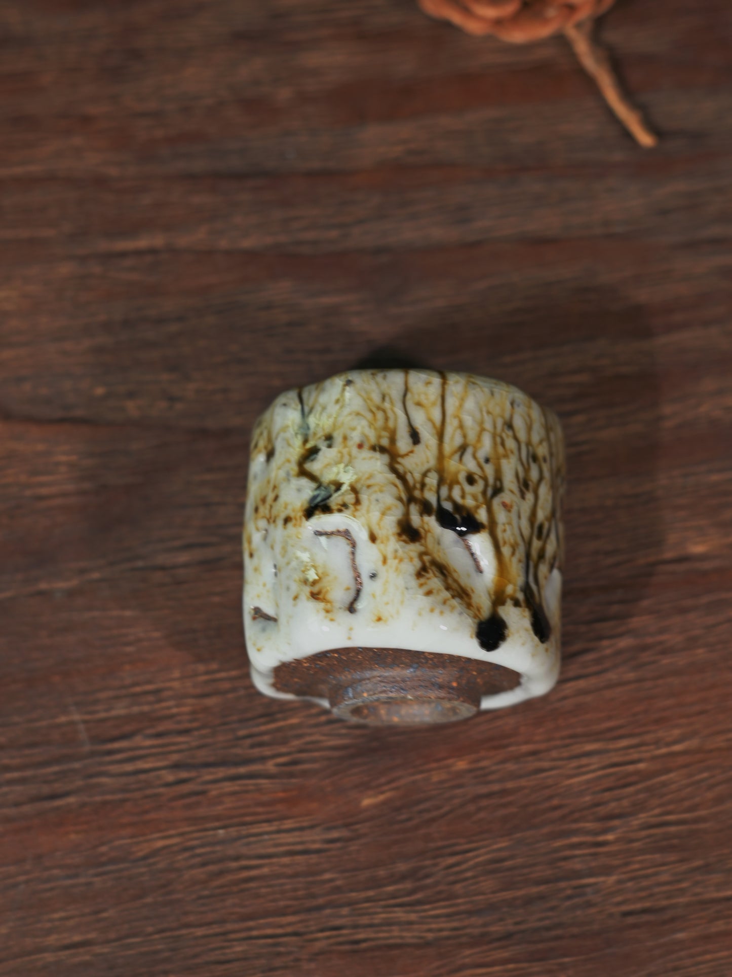 Side view of a 50ml artisan Shino teacup sitting on a traditional carved wooden tea table.