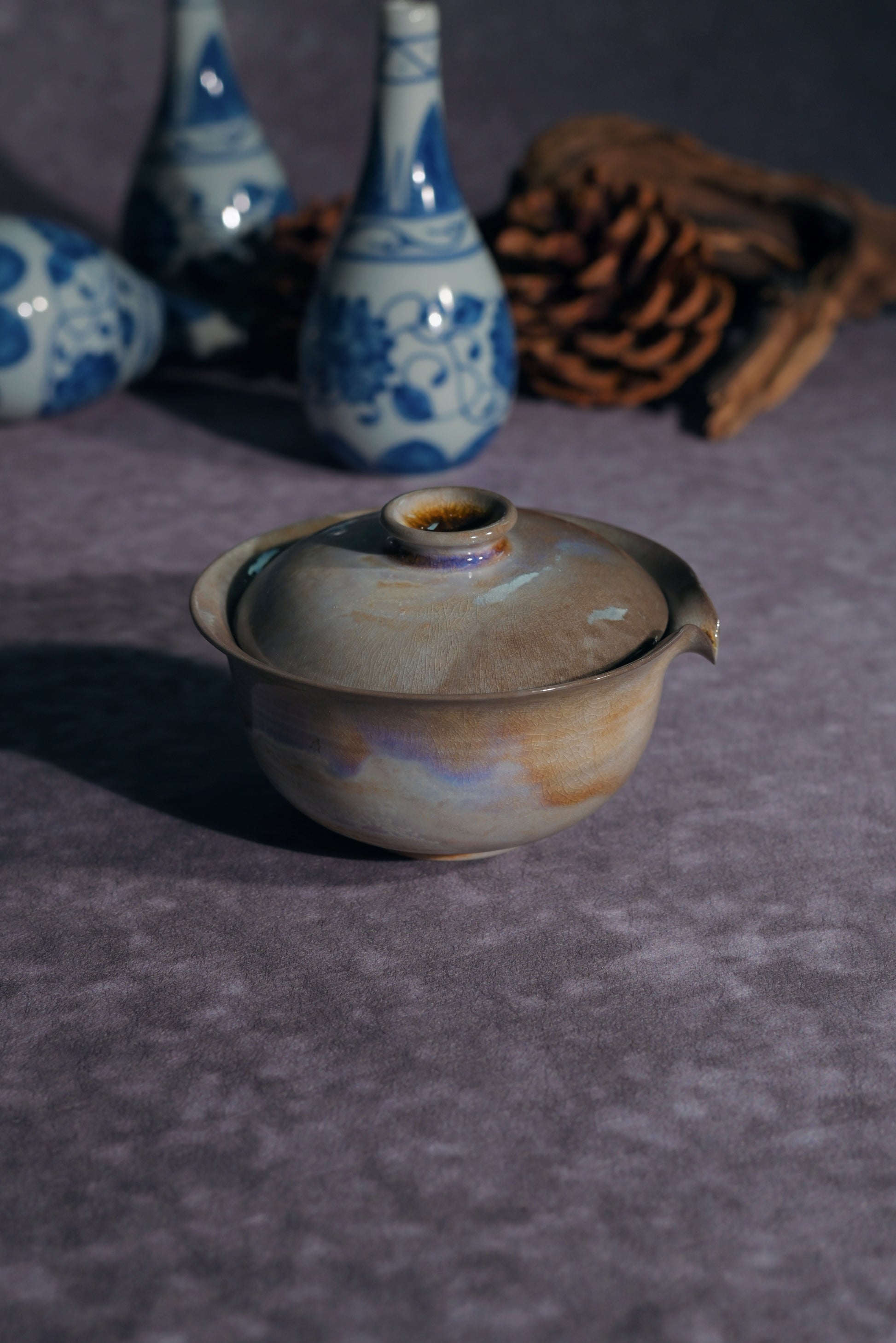Side profile of a shimmering wood-fired Gaiwan reflecting purple and blue hues in the light.