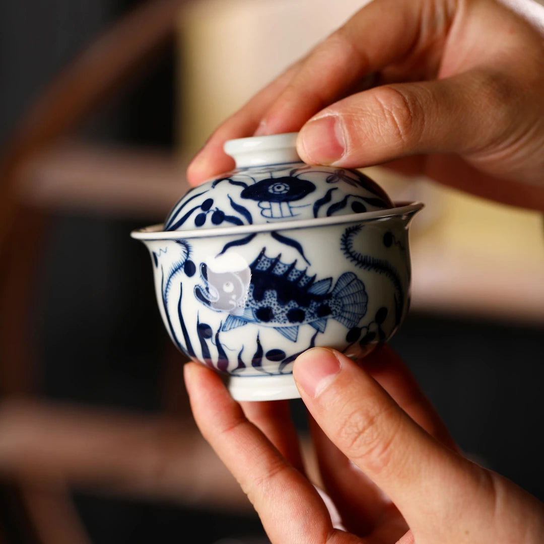 A hand holding the Hand-Painted Blue and White Porcelain Gaiwan to demonstrate its comfortable grip.