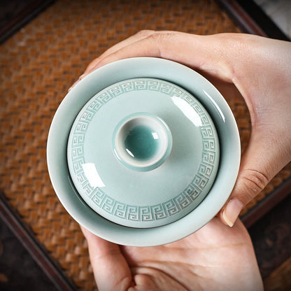 Longquan celadon 180ml gaiwan resting on dark stone tea mat against soft-focus bonsai background