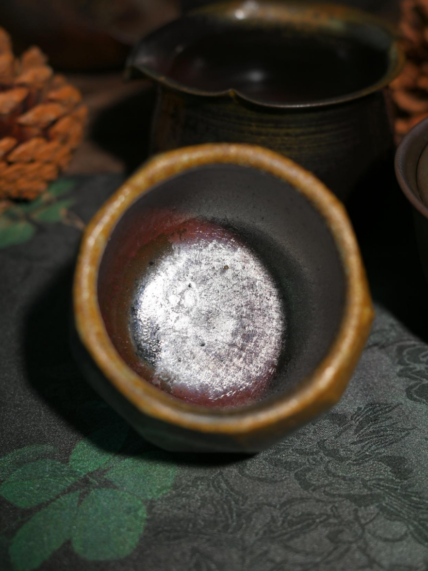 A faceted, hand-carved wood-fired stoneware teacup showcasing rustic Wabi-sabi beauty.