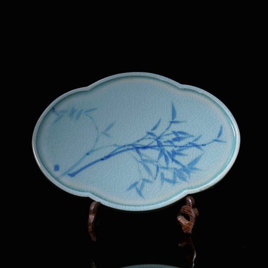 Top view of an antique-style underglaze blue and white porcelain saucer featuring a vintage lattice-window shape, covered in even crackles with a hand-painted bamboo motif at the center.