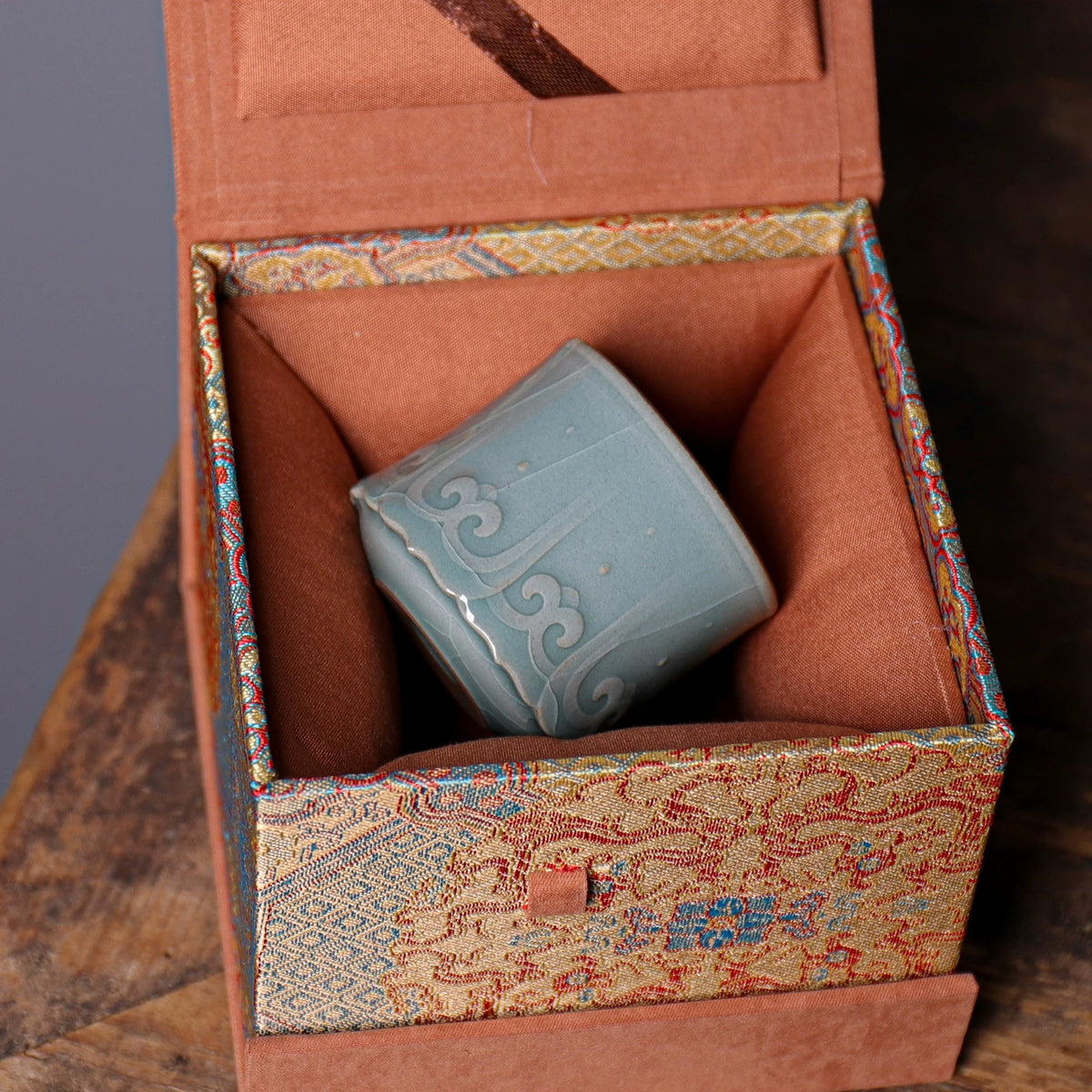 Detailed view of celadon glaze pooling over hand-embossed relief carving on porcelain cup