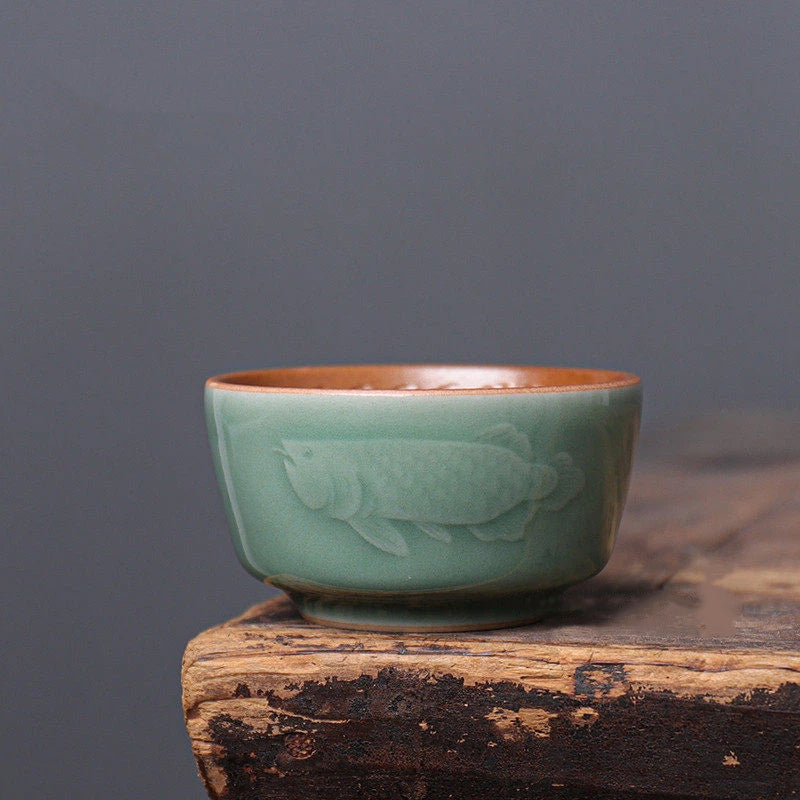 Close-up of the smooth Plum Green glaze and embossed Dragon-Fish motif on the exterior of a celadon cup.