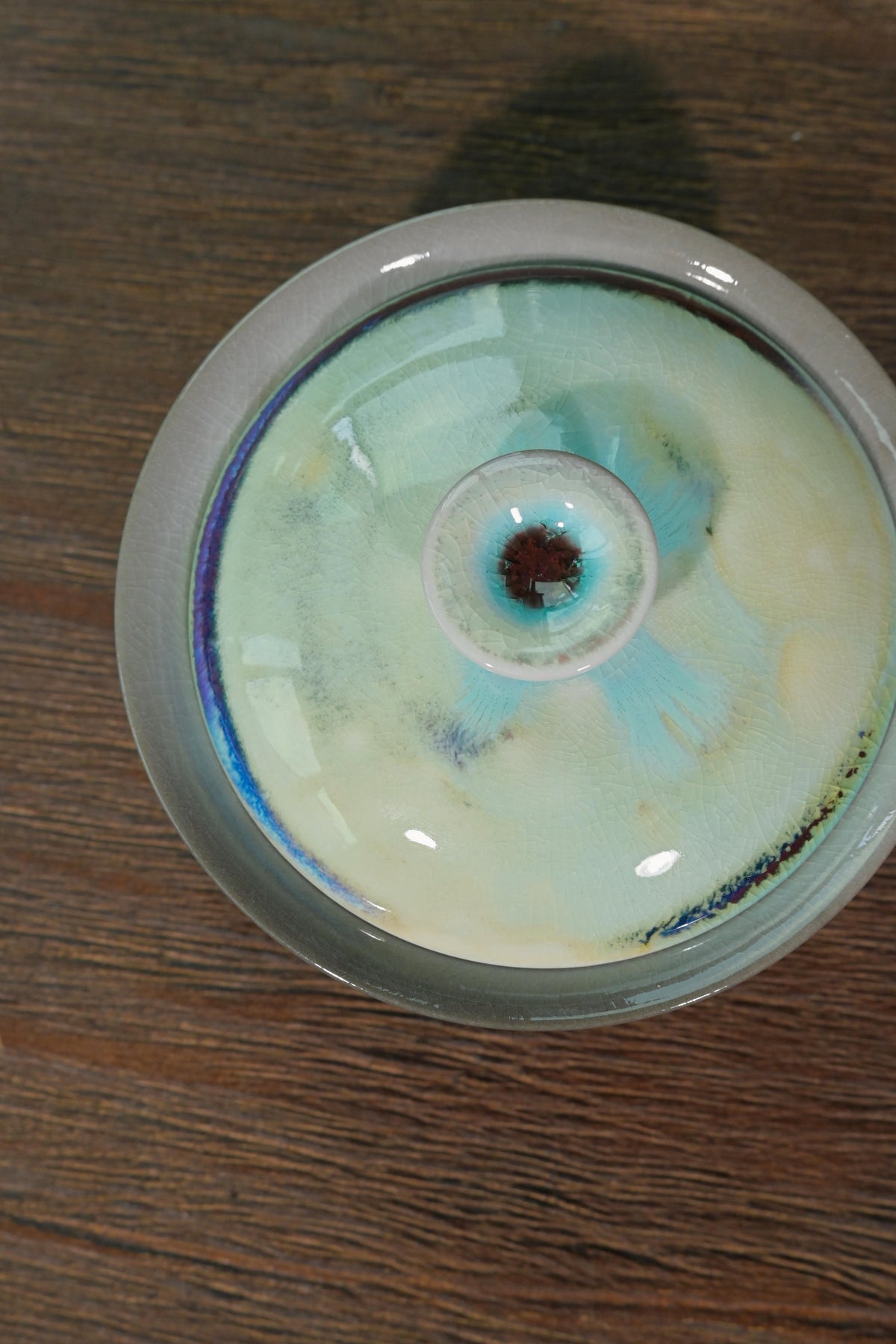 Chashao wood-fired gaiwan displaying electric cyan and violet streak on lid with copper red knob center