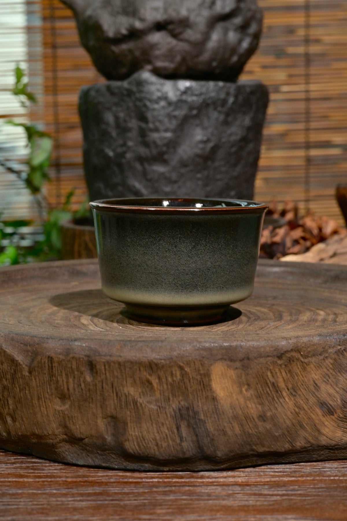 Close-up of Longquan celadon teacup bronze rim and dark iron-rich stoneware foot on rustic wood saucer