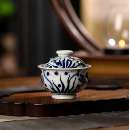 Detailed view of the hand-painted aquatic plants and delicate wave patterns on a blue and white gaiwan.