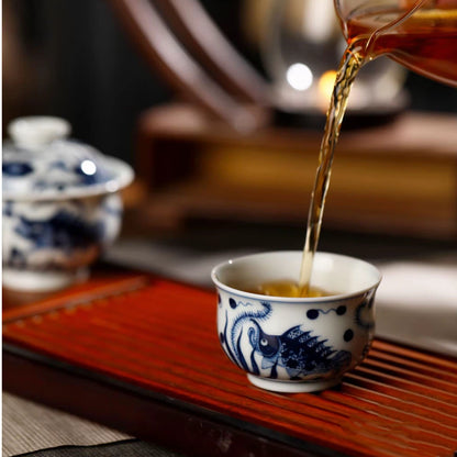 Clear tea liquor being poured smoothly from the flared rim of the blue and white fish gaiwan.