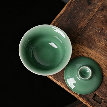 Longquan celadon 150ml three-piece gaiwan set resting on natural wooden tea tray against grey background