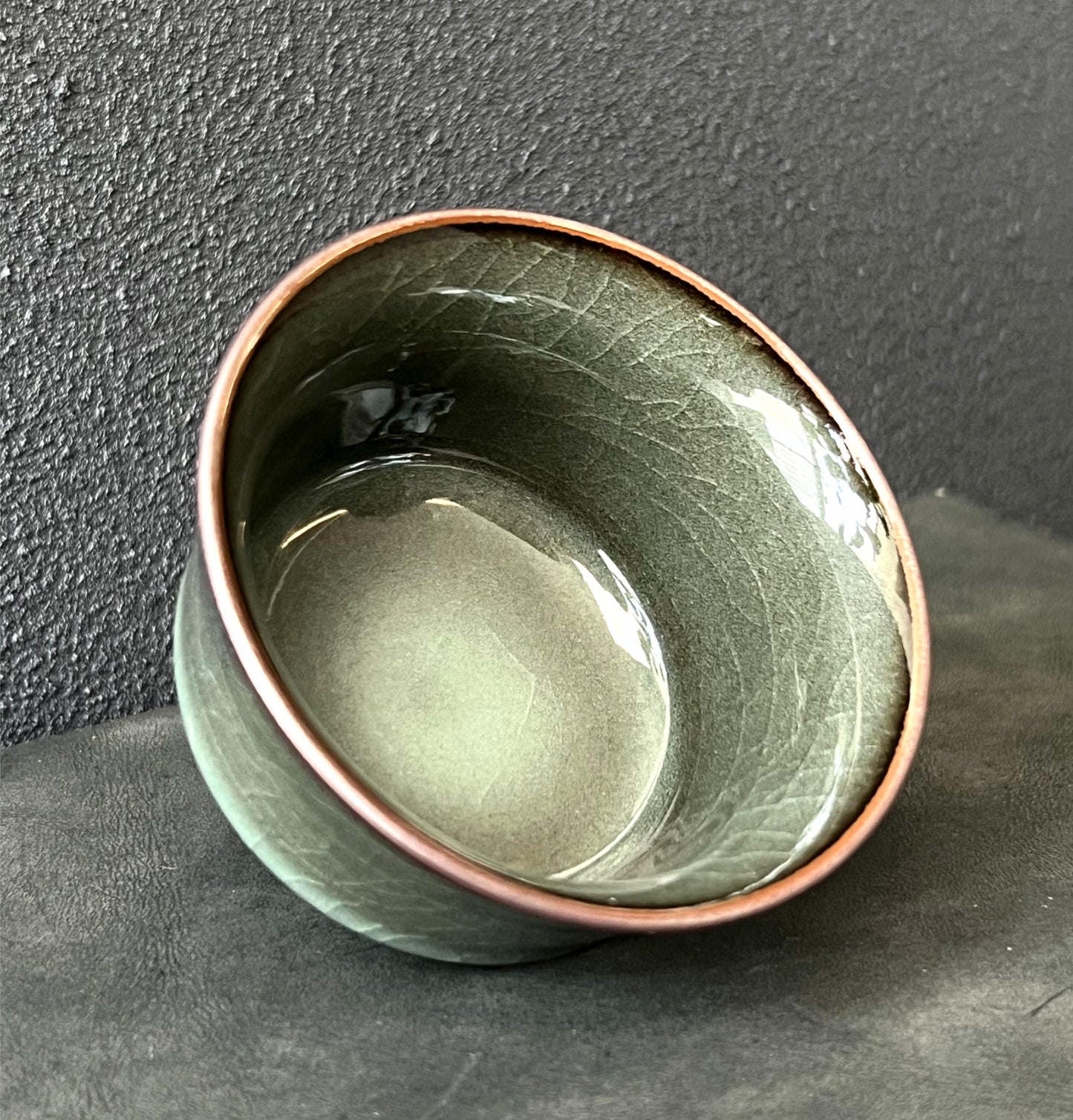 Iron-bodied celadon tea cup featuring a smooth, reflective glaze with fine crackles.