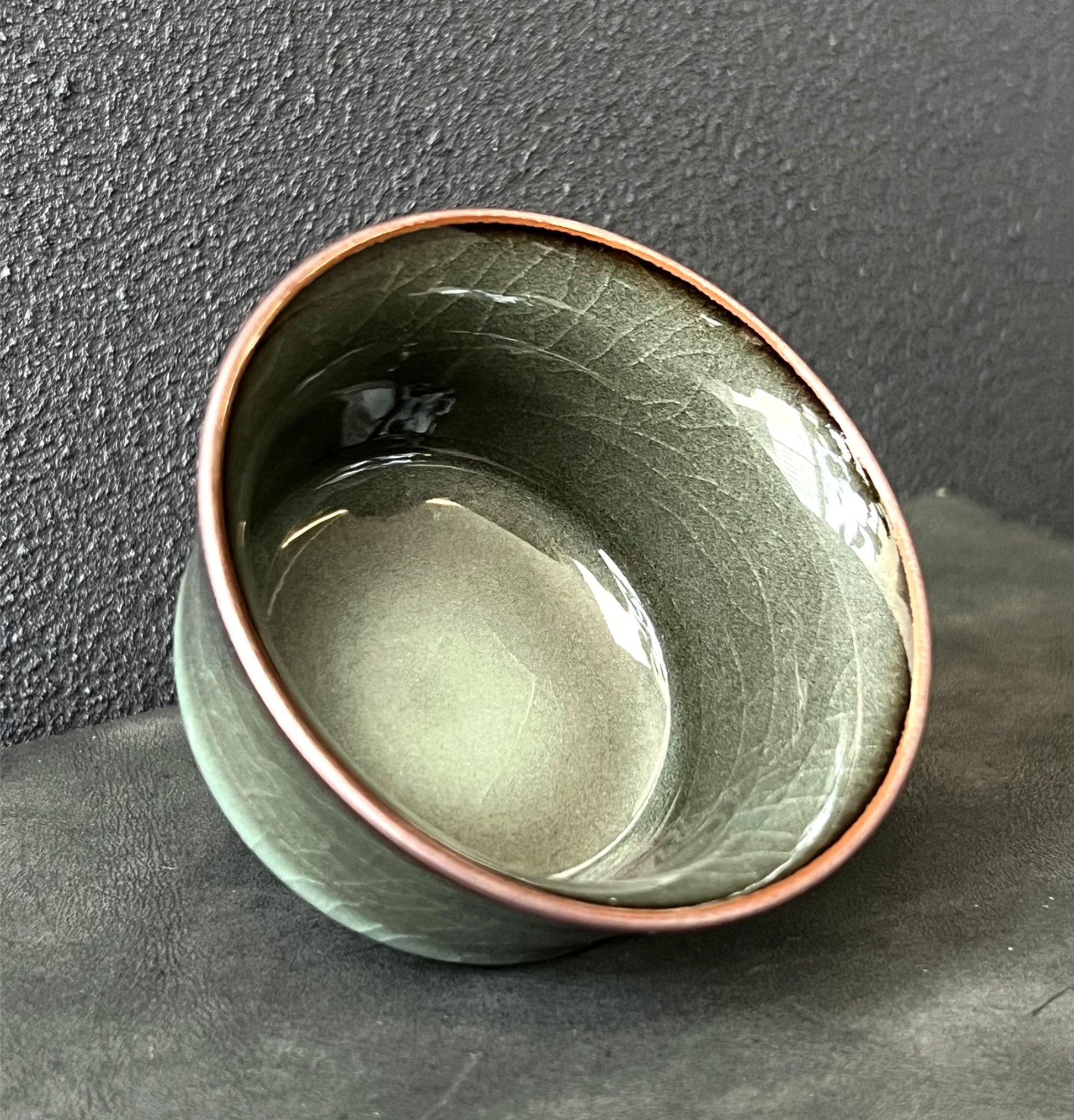 Iron-bodied celadon tea cup featuring a smooth, reflective glaze with fine crackles.