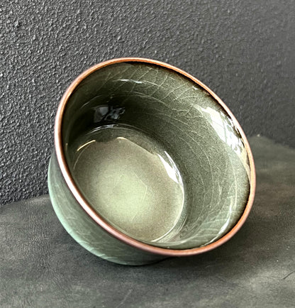 Iron-bodied celadon tea cup featuring a smooth, reflective glaze with fine crackles.