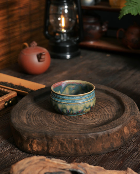 Handmade Jun ware drum-belly cup showing flowing red, purple, and blue glaze