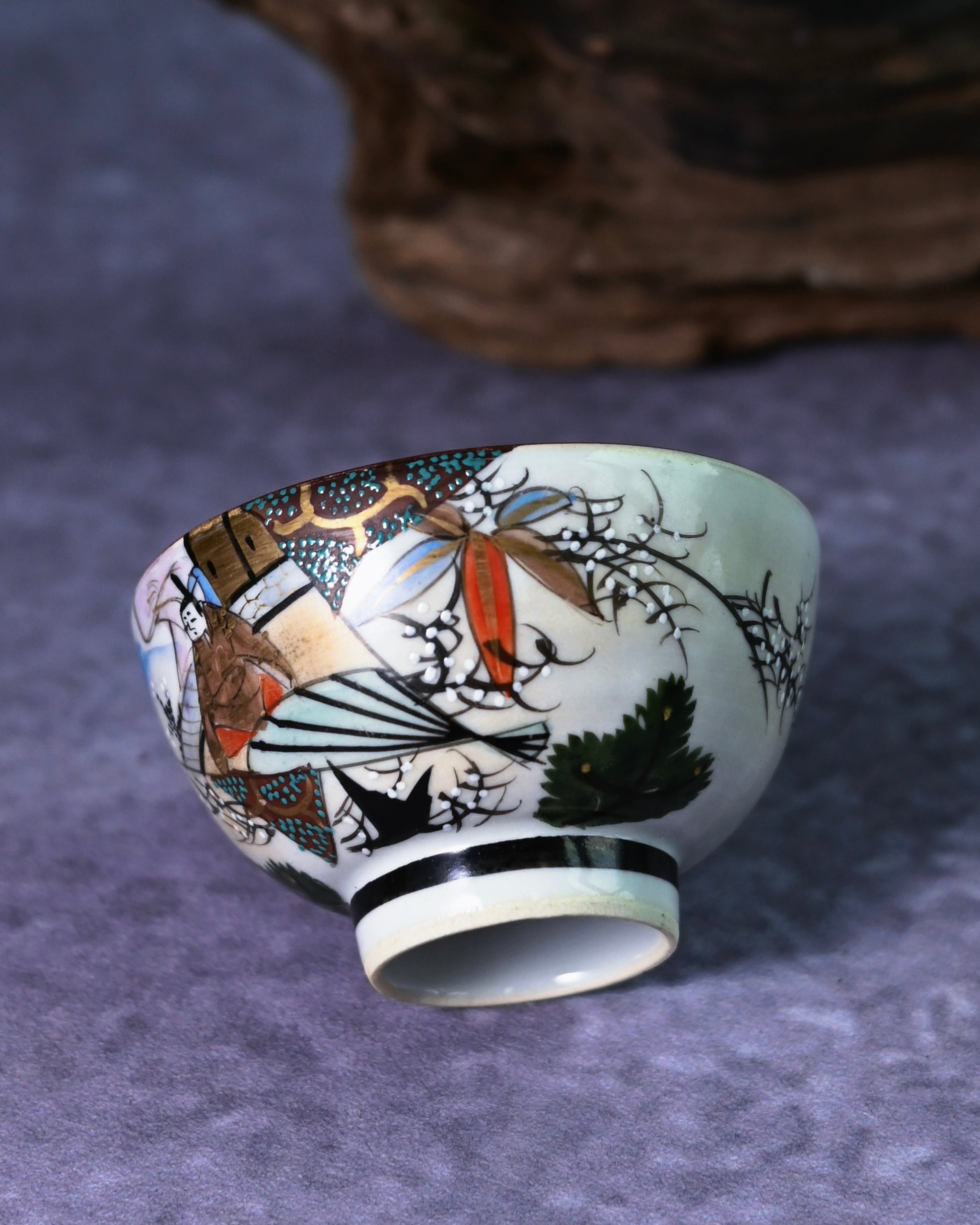 Hand-painted Ukiyo-e style figure on a Kutani tea cup, dressed in traditional kimono with bold red, gold, and black enamel colors.