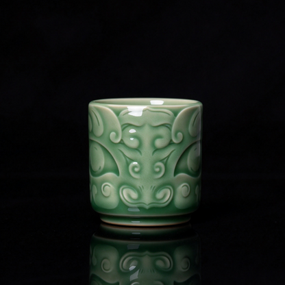 Longquan Celadon ancient bronze Taotie mask embossed relief teacup with jade green glaze resting on wooden block