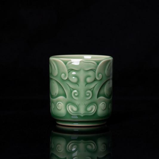 Longquan Celadon ancient bronze Taotie mask embossed relief teacup with jade green glaze resting on wooden block