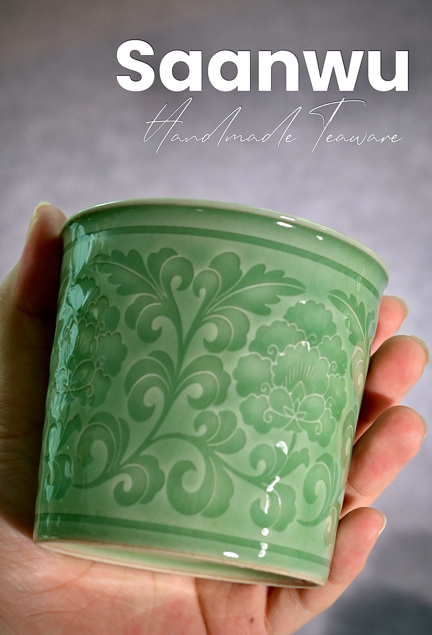 A hand holding the Longquan Celadon Peony Relief Cup, showing its comfortable ergonomic grip.