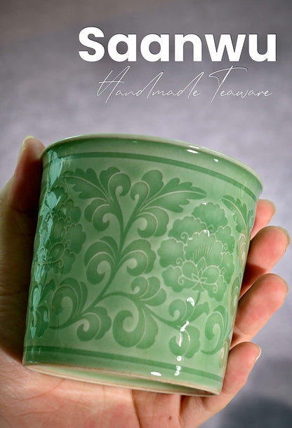 A hand holding the Longquan Celadon Peony Relief Cup, showing its comfortable ergonomic grip.