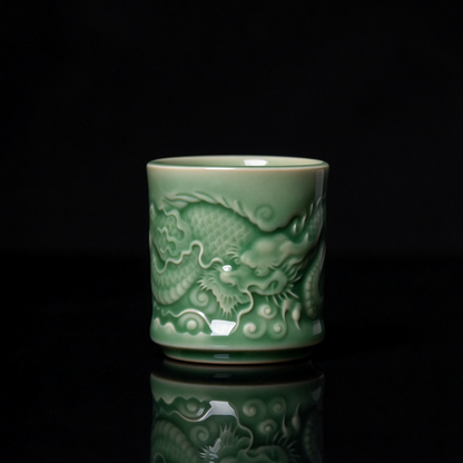 Longquan Celadon imperial dragon embossed relief teacup with jade green glaze resting on wooden block