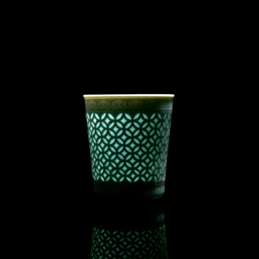 Handmade tall Longquan celadon linglong tea cup with hollow coin lattice translucent craft, black reflective background oriental tea ware