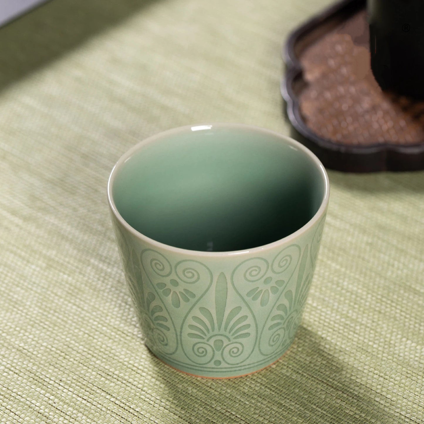 Close-up of the vibrant plum green celadon glaze and relief carved pattern on a ceramic cup.