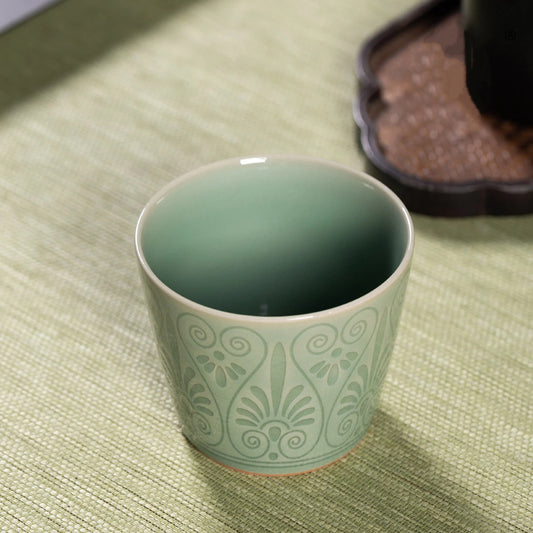 Close-up of the vibrant plum green celadon glaze and relief carved pattern on a ceramic cup.