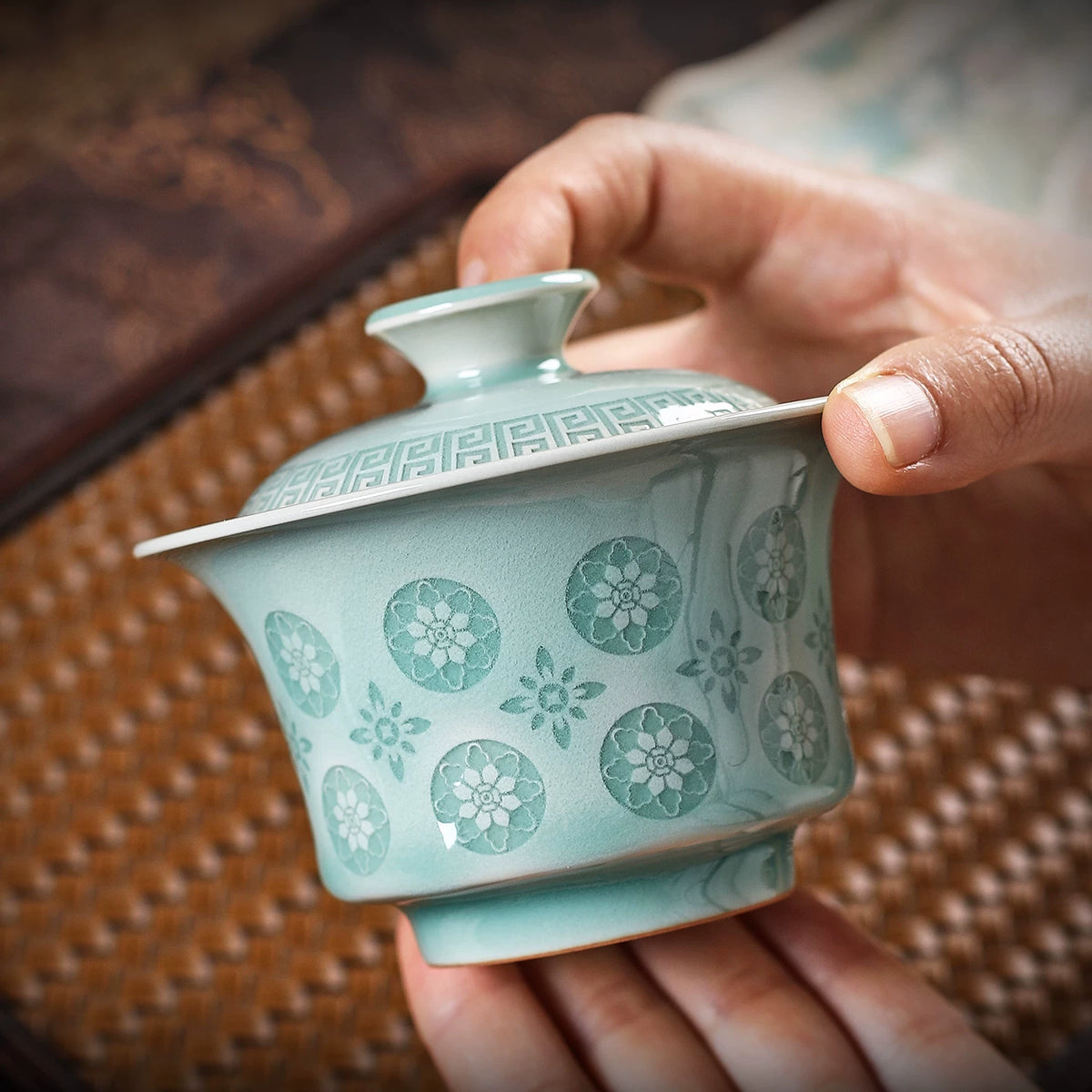 Close-up of powder green celadon gaiwan lid and bowl showing jade-like glaze melt over carved relief details