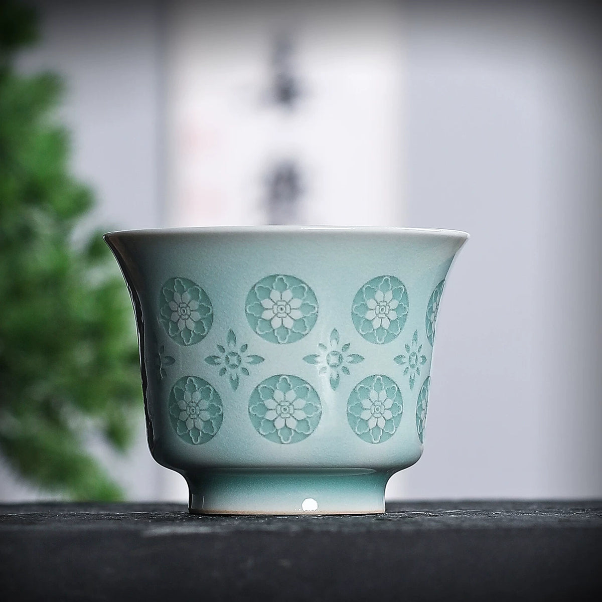 Close-up of powder green celadon horse-hoof cup rim and glowing pierced flower cutouts under ambient light