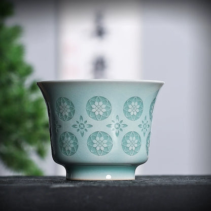 Close-up of powder green celadon horse-hoof cup rim and glowing pierced flower cutouts under ambient light