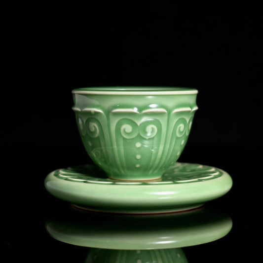 Longquan celadon teacup with saucer featuring plum green glaze and hand-carved Baoxiang pattern inspired by Song Dynasty ceramics.