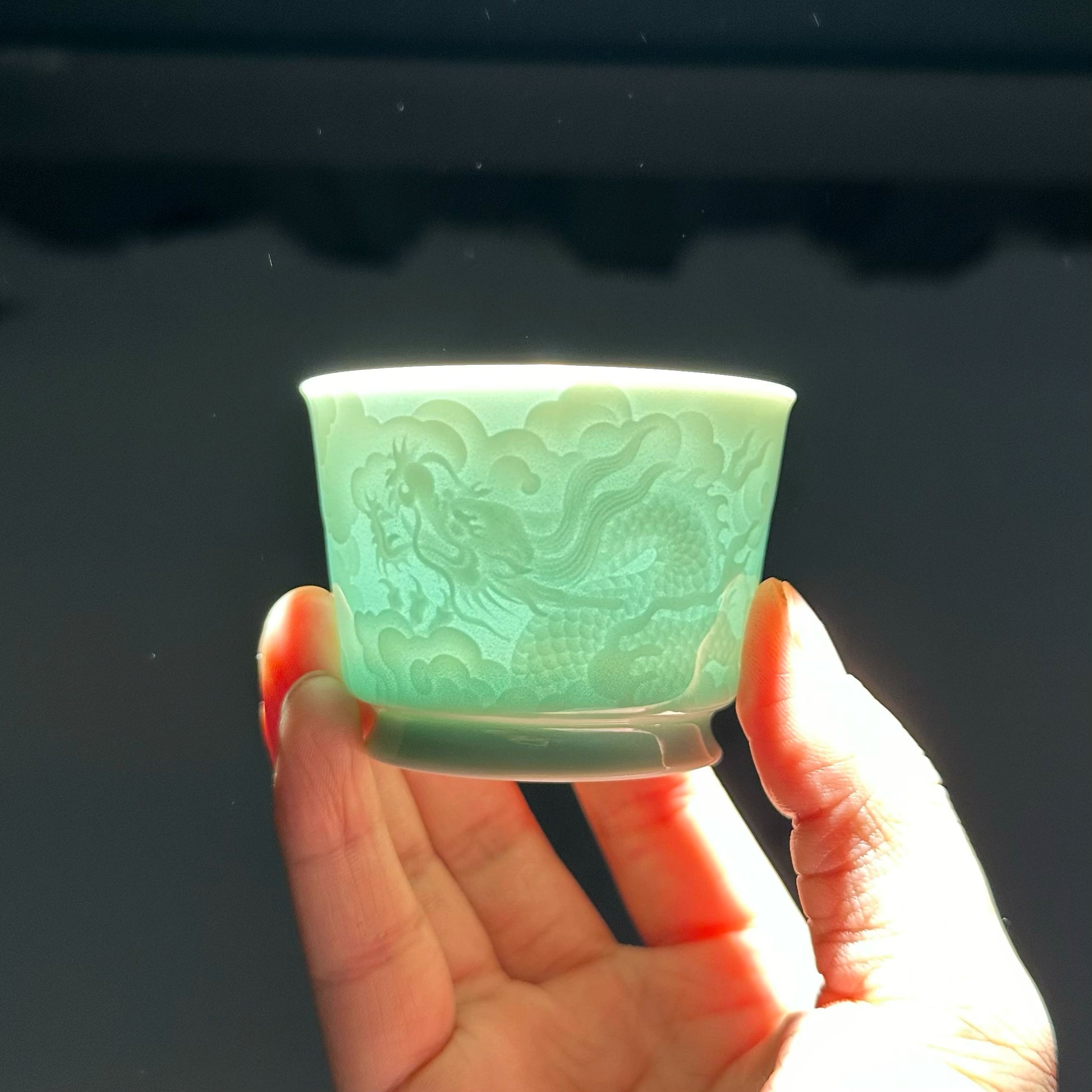 Backlit view showing the light-transmitting quality of the translucent Longquan Celadon relief carved tea cup.