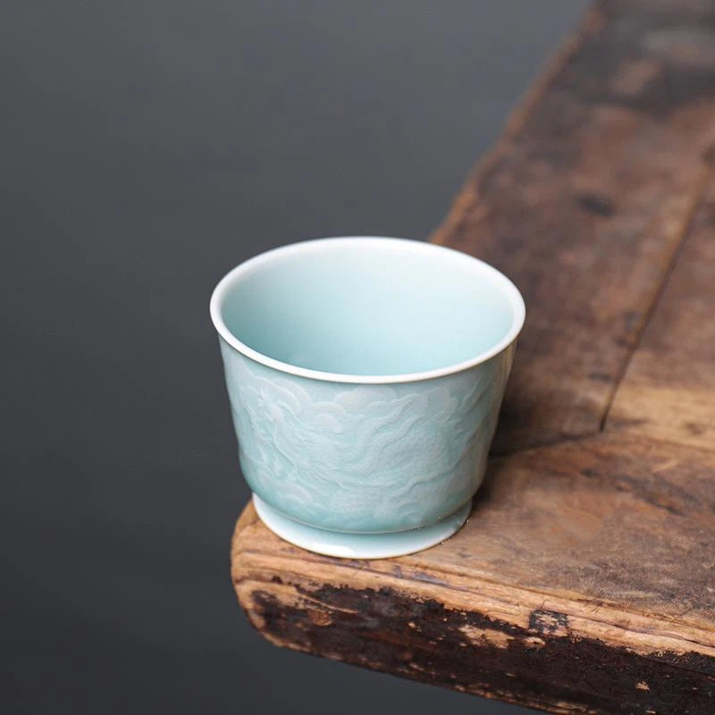 Longquan Celadon Translucent Relief Carved Tea Cup set on a wooden tea tray alongside Gongfu tea accessories.