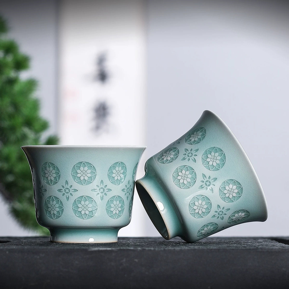 Longquan celadon horse-hoof teacup resting on rustic tea mat against dark background
