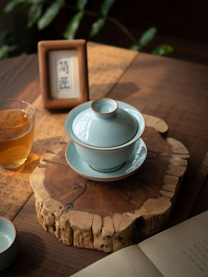 Handcrafted Ru Kiln sky-blue porcelain gaiwan and two teacups set with bronze rims resting on a wooden tray