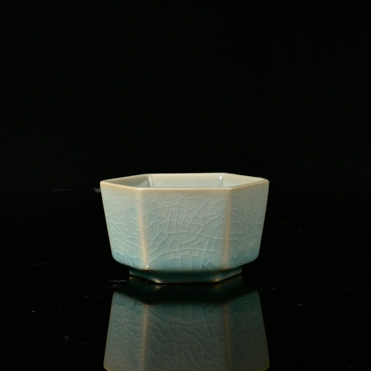 Ru Ware sky-blue glazed hexagonal master teacup resting on reflective dark surface