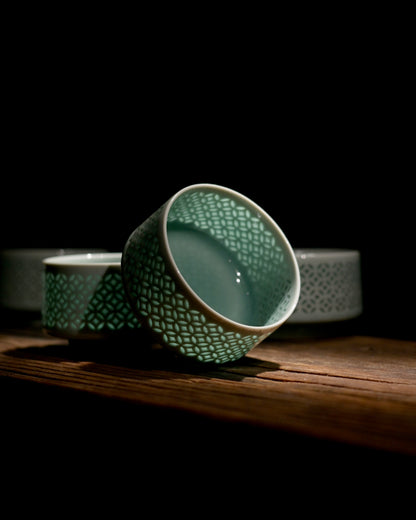 Product shot linglong Longquan celadon tea cup on black mirror reflective background, hollow coin mesh translucent ceramic cup