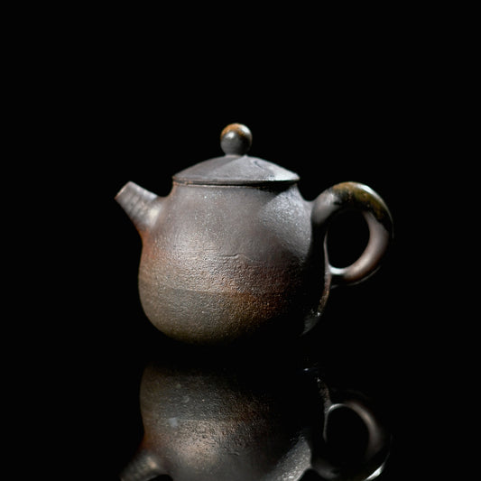 Unique piece artisan hand-thrown iron clay teapot with a dark metallic texture on a reflective surface.