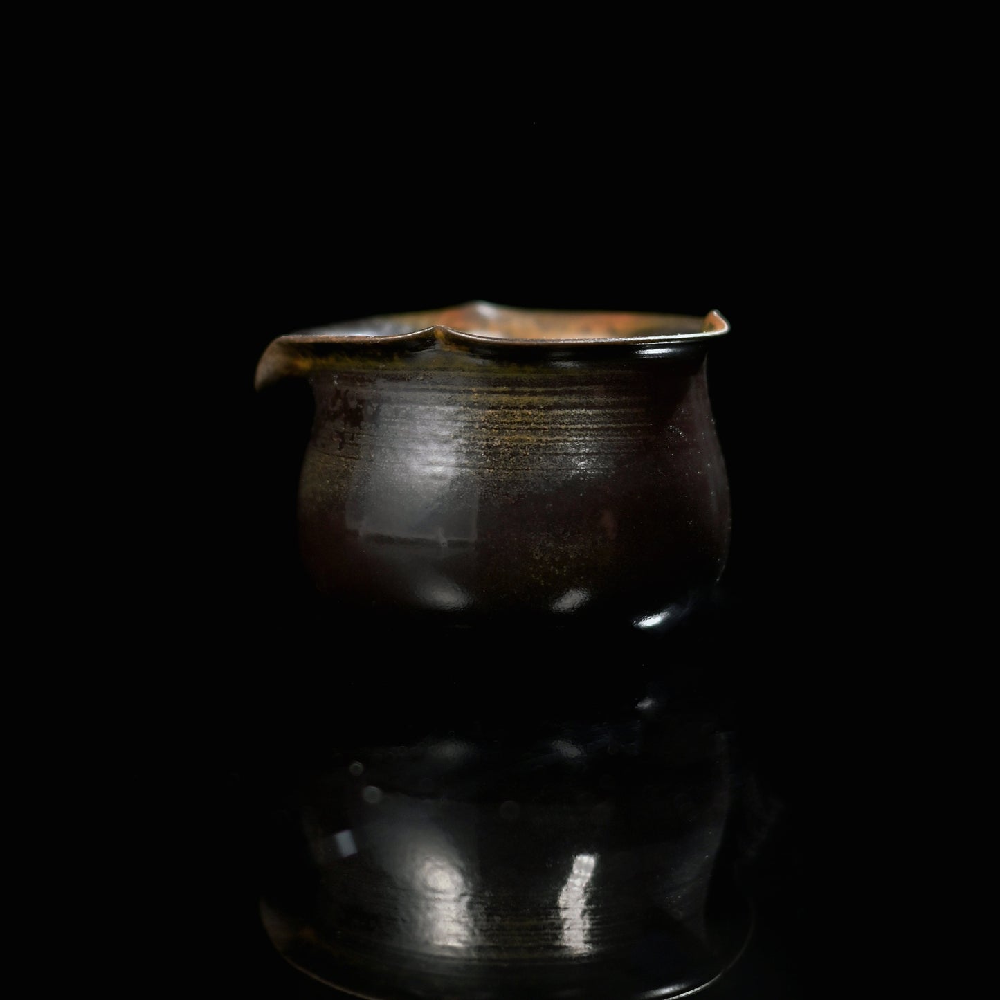 Unique piece wood-fired black gold mud fairness cup on a rustic wood slice against a green backdrop.