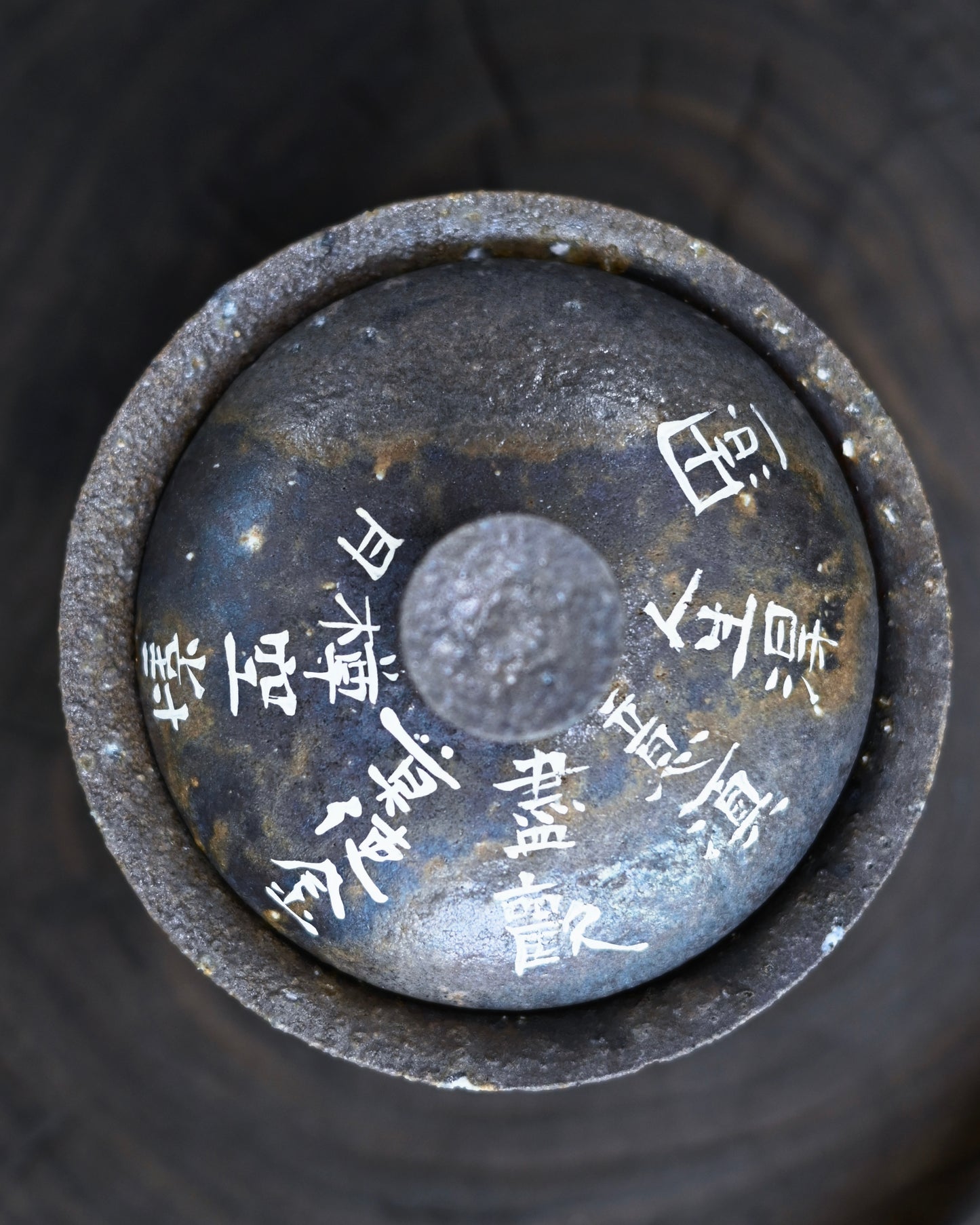 Wabi-sabi tea bowl showing natural fire marks, visible grit particles, and dark pigment cursive script on warm gray-brown clay