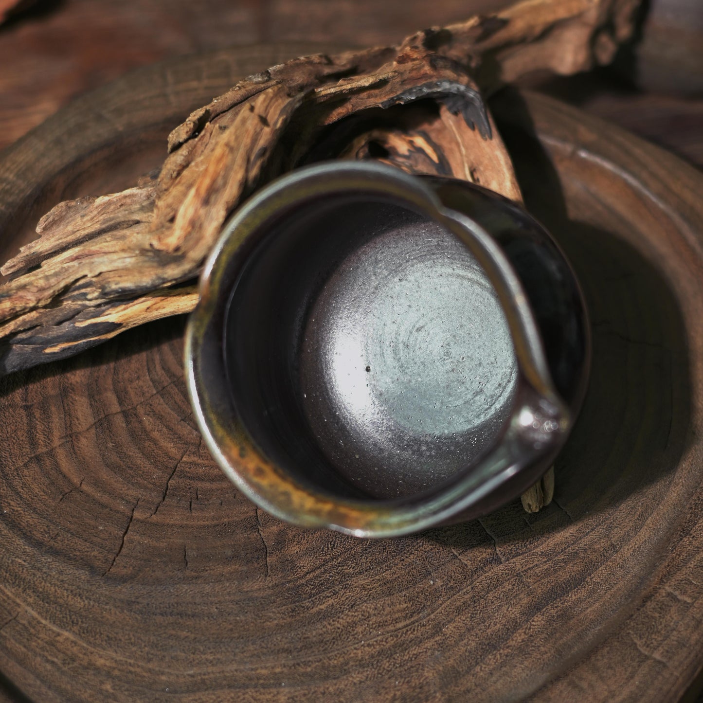 Side profile of the unique hand-shaped black gold mud fairness cup in a rustic setting.