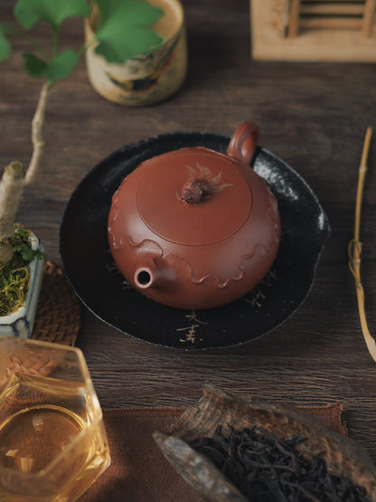 Yixing master-crafted zhuni teapot featuring delicate hand-carved lotus blooms, refined flattened Xishi shape, and exceptionally smooth pouring performance.