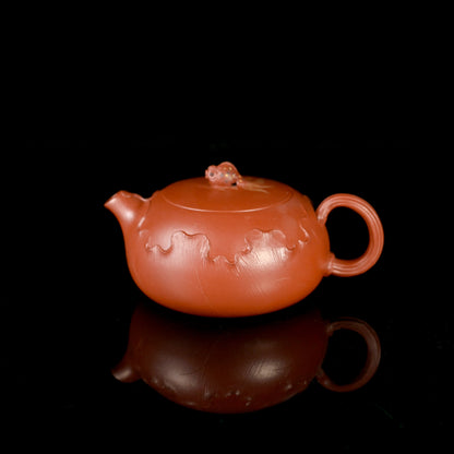 Yixing zisha Xishi teapot in vibrant zhuni clay, featuring hand-carved lotus motifs and flawless pouring performance, fully handcrafted in the elegant flattened Xishi form.